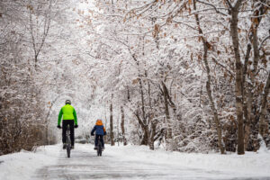 A father and his son ride a bikes in a winter park. Back view. Weekend in a snowy park. The source: rrc.ca.
